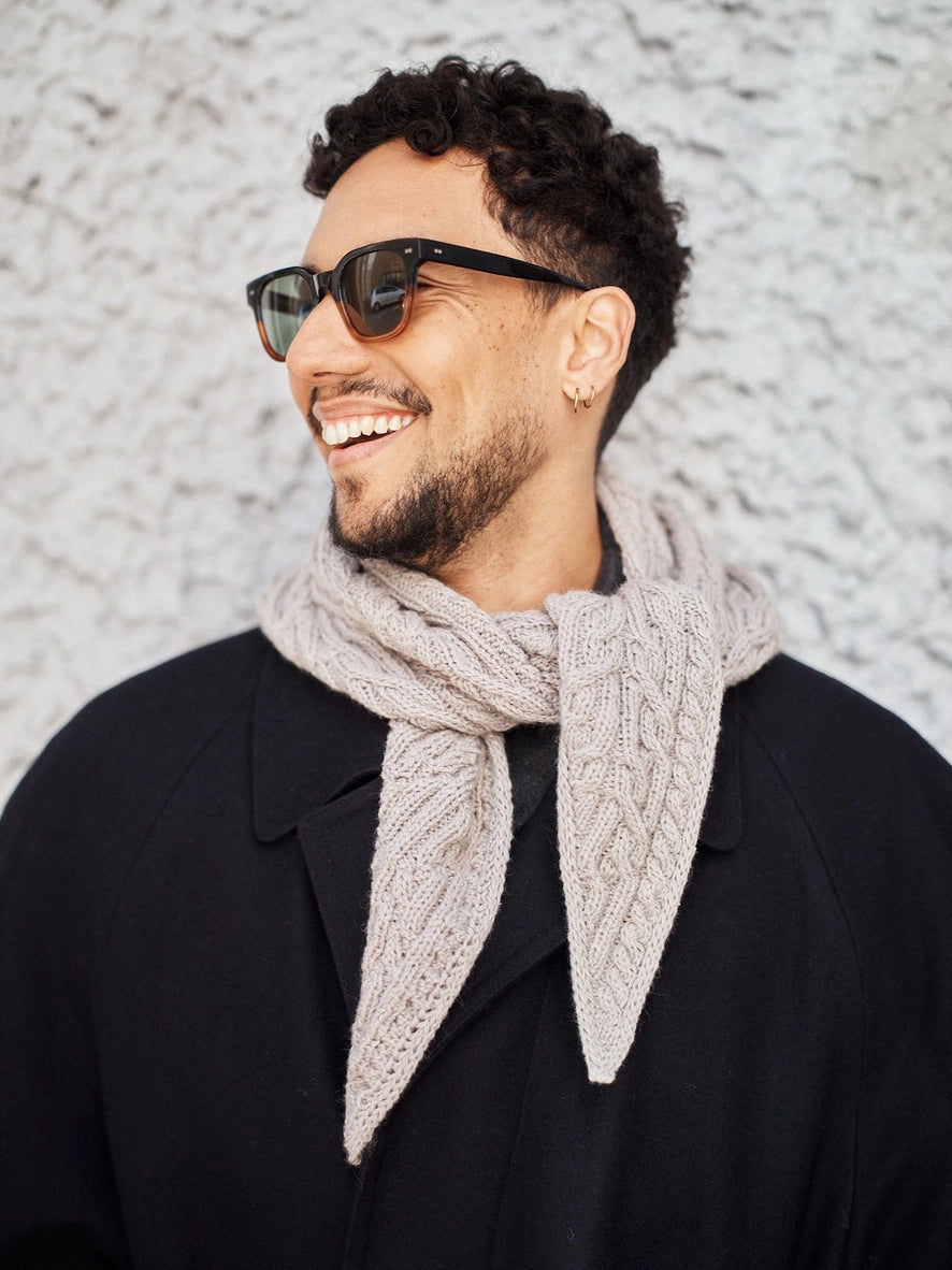 Man wearing sunglasses and a beige scarf against a textured wall