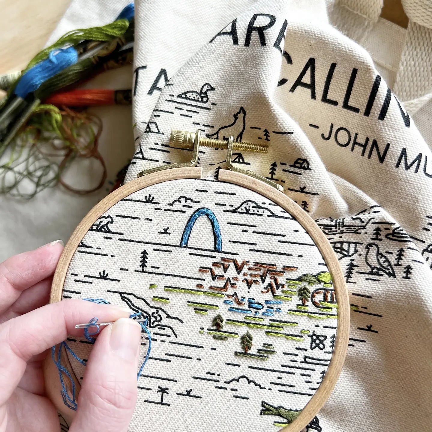 Embroidery hoop with a partially completed landscape design on fabric.