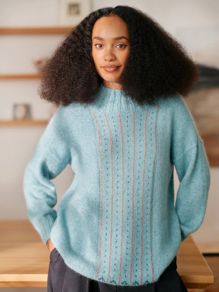 Woman wearing a light blue sweater with a textured pattern in a kitchen setting