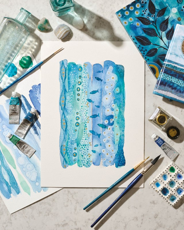 Artistic watercolor painting of blue and green abstract patterns with art supplies on a textured surface.