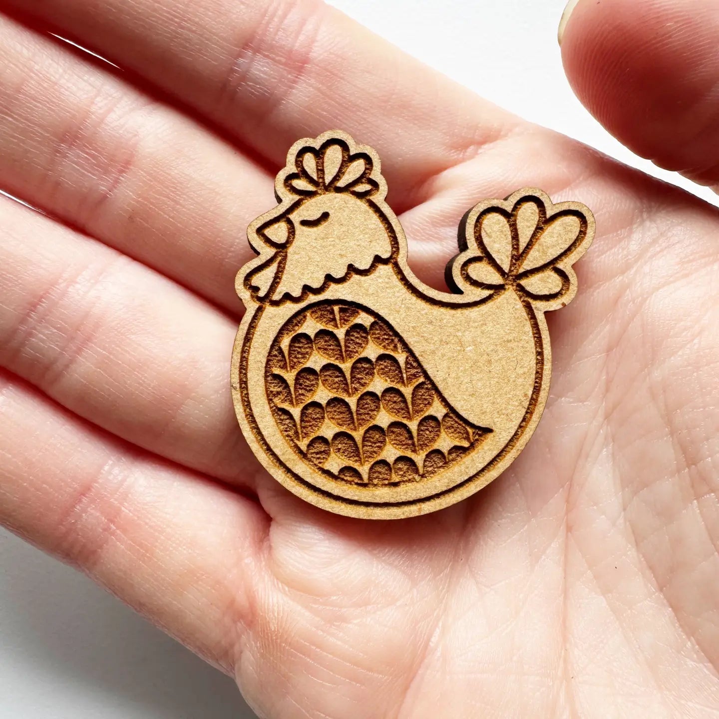 Wooden chicken-shaped stamp held in a hand against a white background