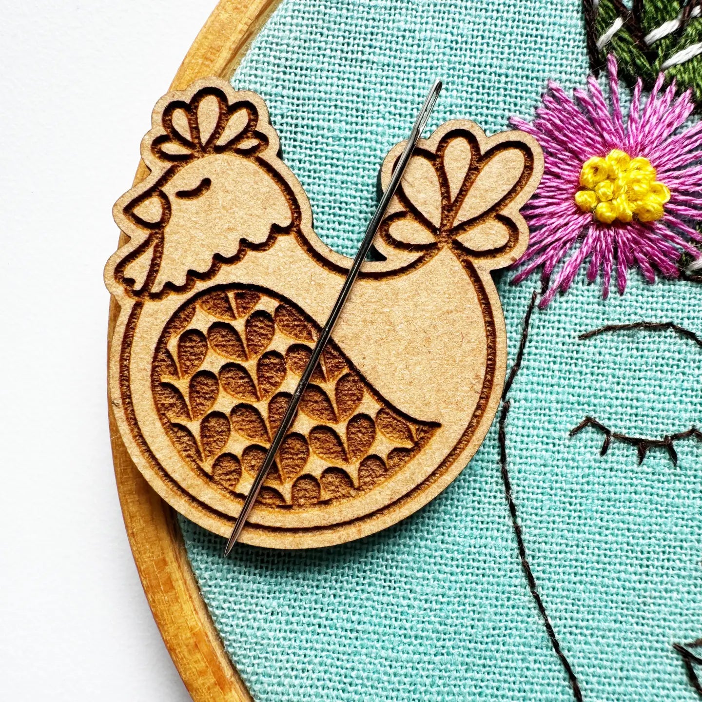 Wooden chicken-shaped embroidery hoop with a needle on a fabric background