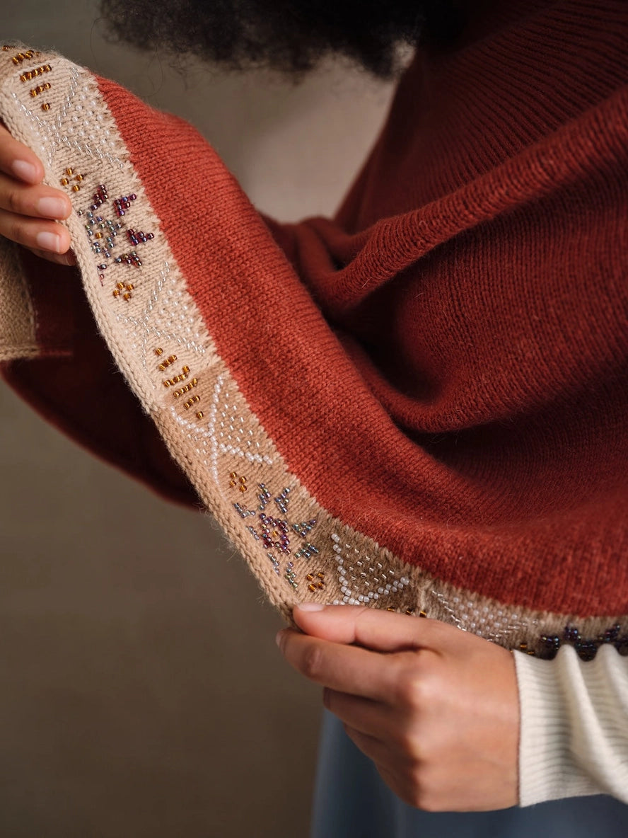 Person wearing a red sweater holding a piece of beaded embroidered.