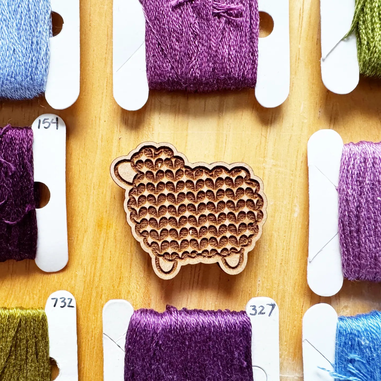 Wooden sheep-shaped tool on a wooden board with spools of thread in various colors.