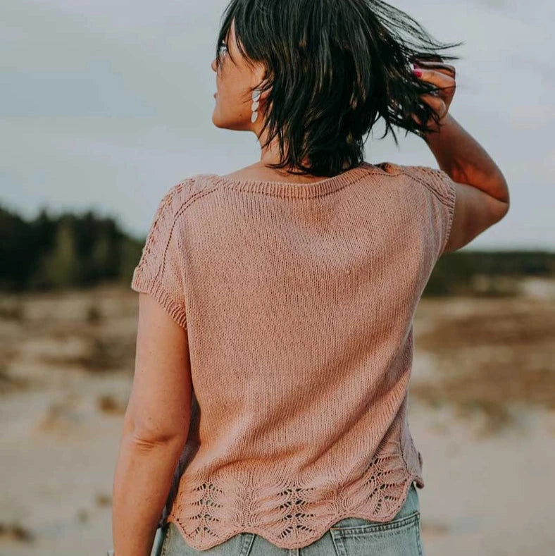 Person wearing a pink sleeveless top and denim shorts on a beach.