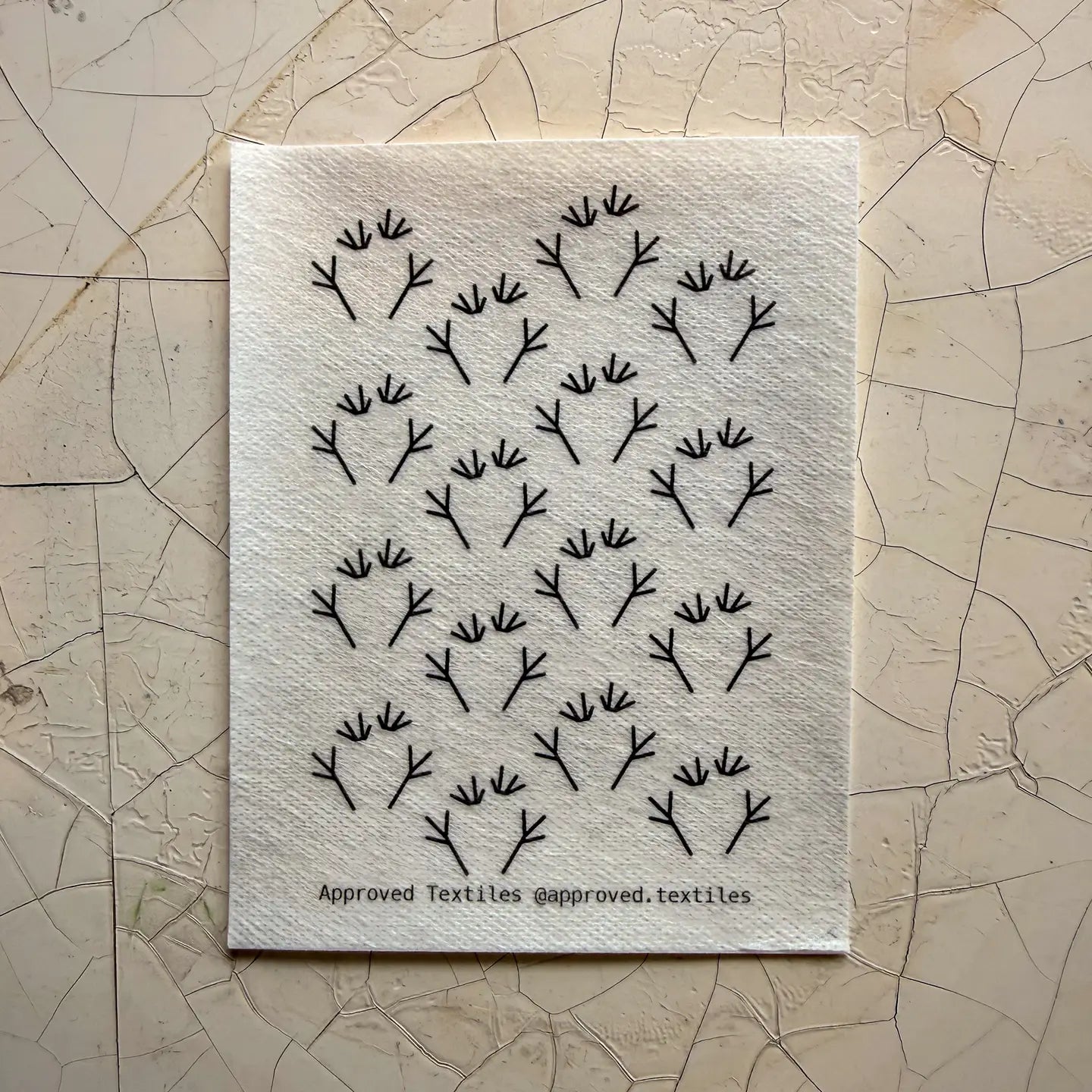 Textile sample with black frog feet pattern on a textured beige background