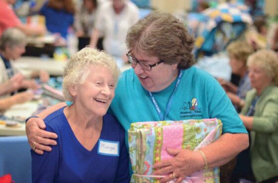 Two women hugging with a quilt at a craft fair